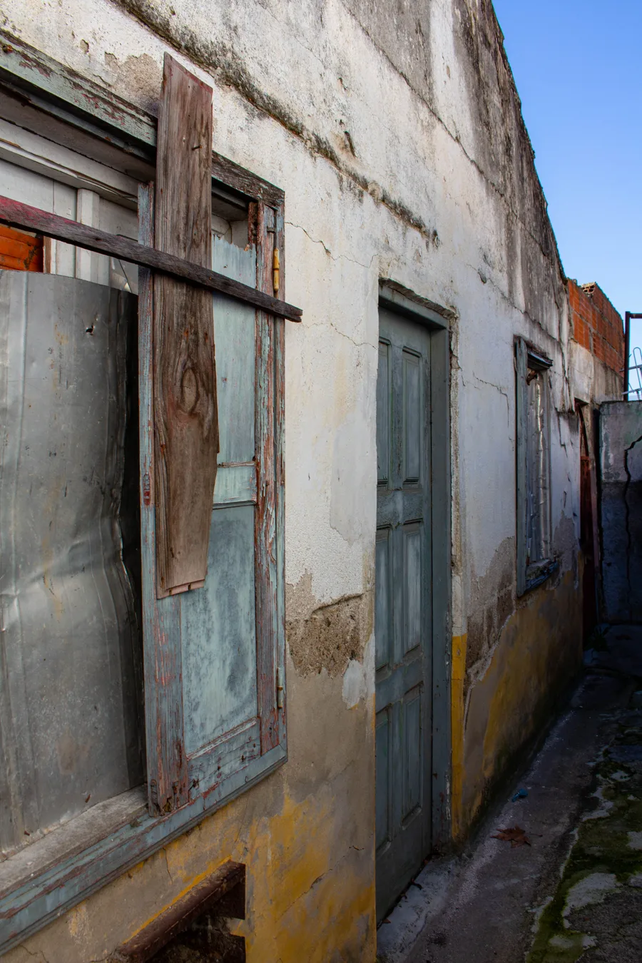 South-facing facade with a decayed window and a loose wooden board, diagonal alignment