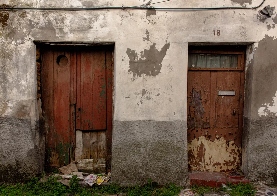 Two weathered red-brown doors side by side on a house numbered 18