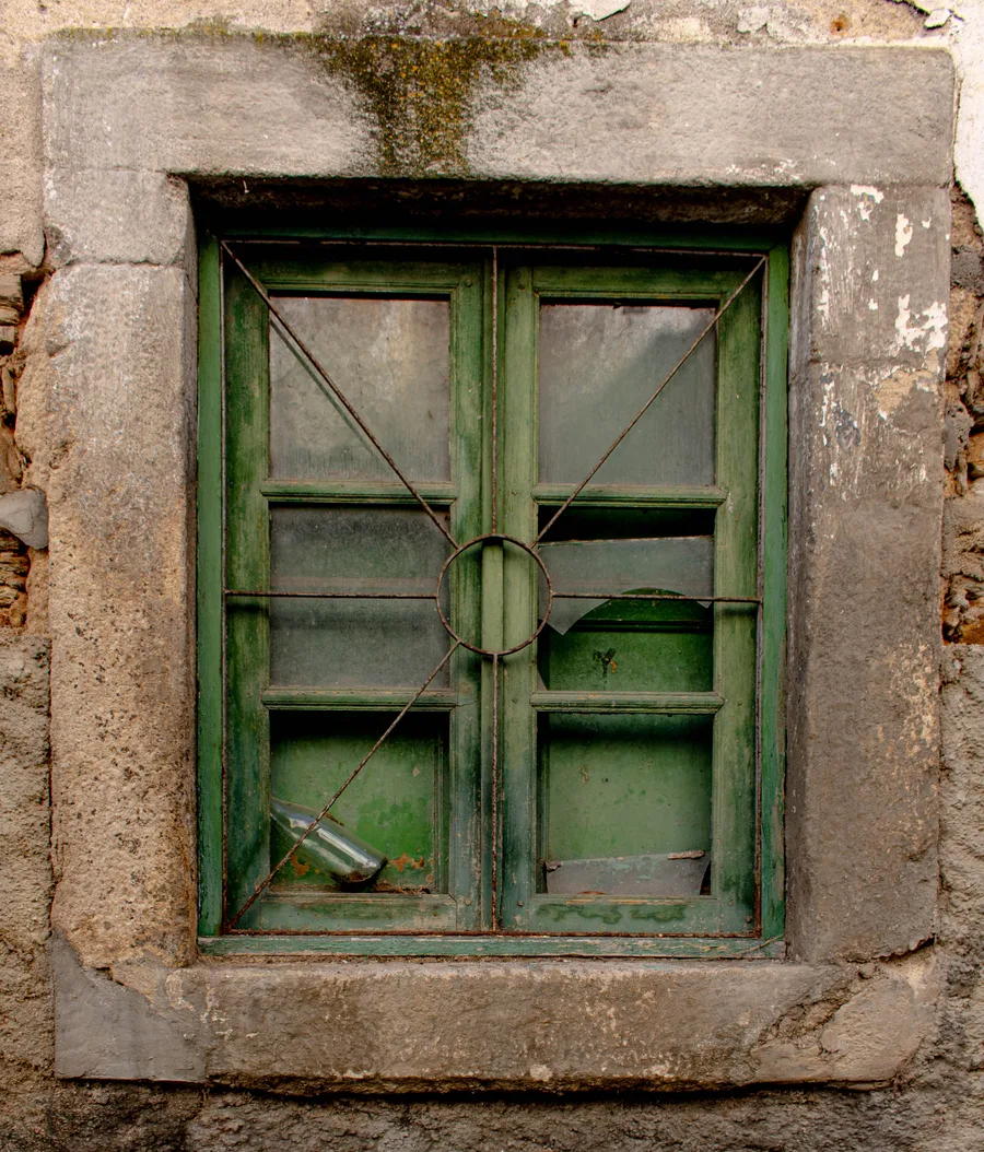 Green-framed window with a cross-brace iron grille and a bottle wedged inside