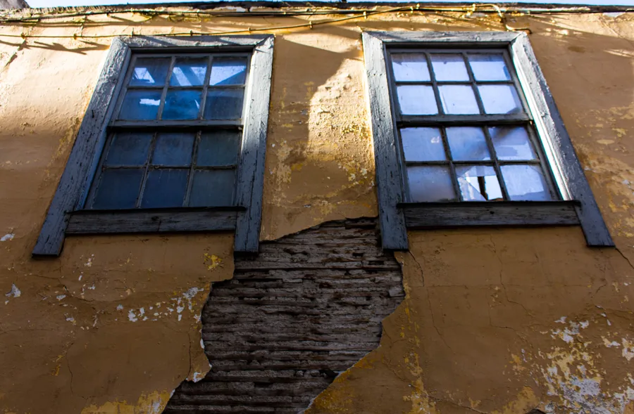 Two symmetric windows on a mustard-yellow facade, low angle, cracked wall between them