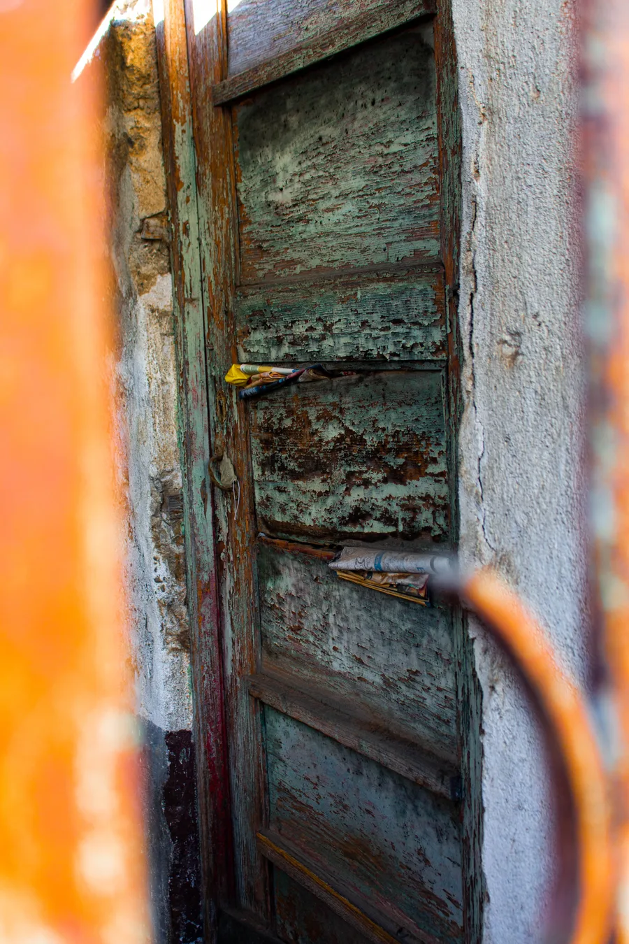 Oxidised green door with an orange cable and newspaper wedged in it