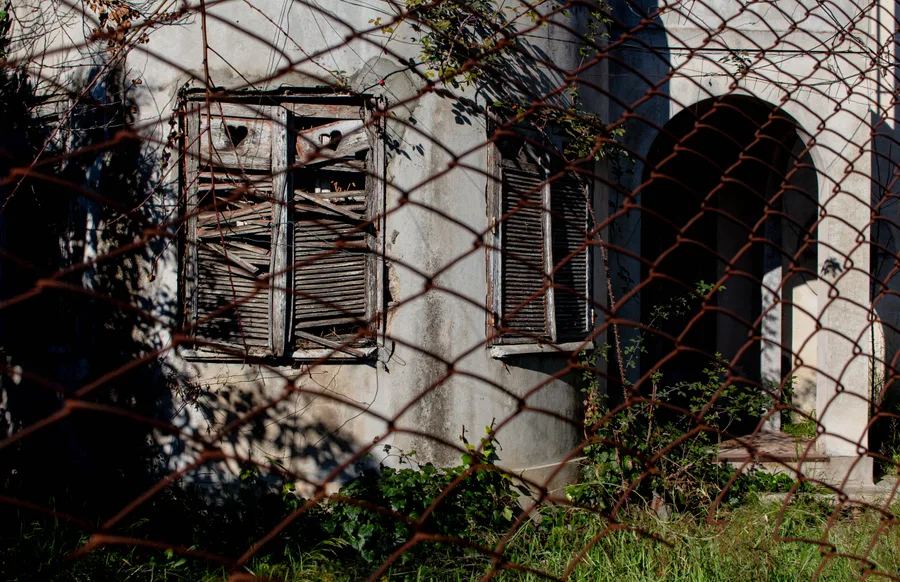 Abandoned building behind a wire fence, arched doorway visible