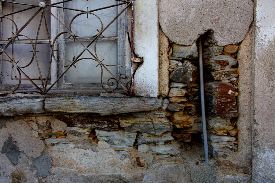 Ornate wrought-iron window grille beside an exposed stone wall corner